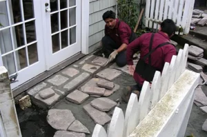 Workers laying stone pathway near house entrance.