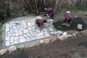 Workers laying stone pavement in garden.
