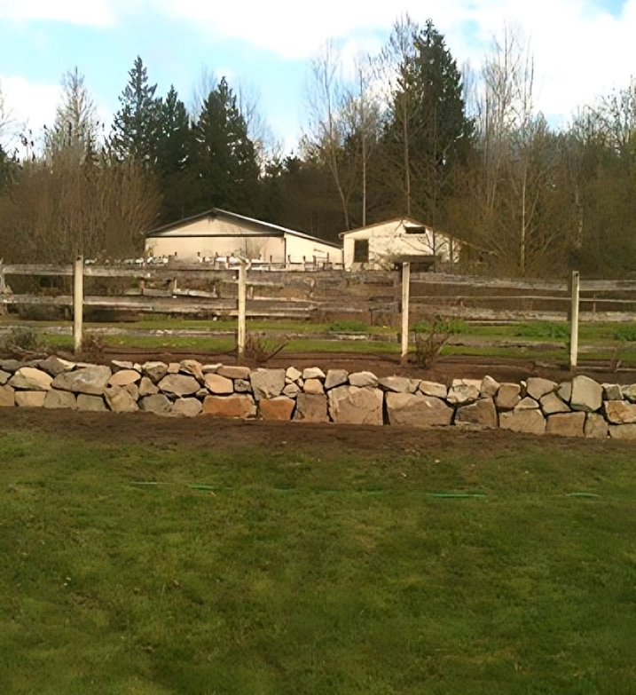 Rock wall, wooden fence, rural landscape, trees.