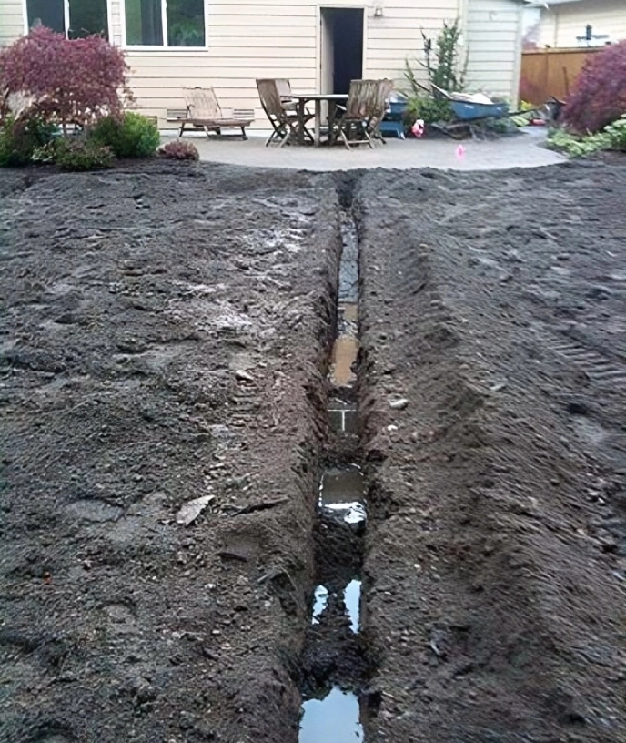 Trench dug in backyard near patio area.