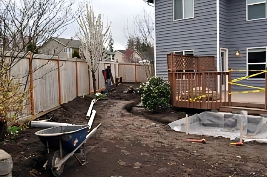 Backyard under construction with wheelbarrow and deck.