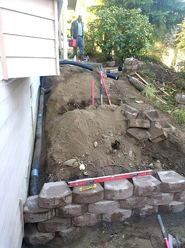 Garden retaining wall construction with tools visible.